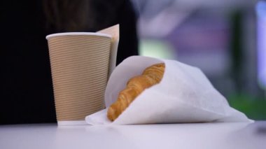 Lezzetli, taze kruvasanlar. Kağıt bardakta kahve, bulanık arka planda kadınların elinde..