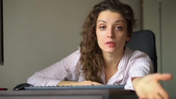 Giovane donna stanca con i capelli ricci e camicia bianca sta lavorando in ufficio utilizzando il suo computer portatile, lavoro di routine, freelance, sindrome di burnout — Video Stock