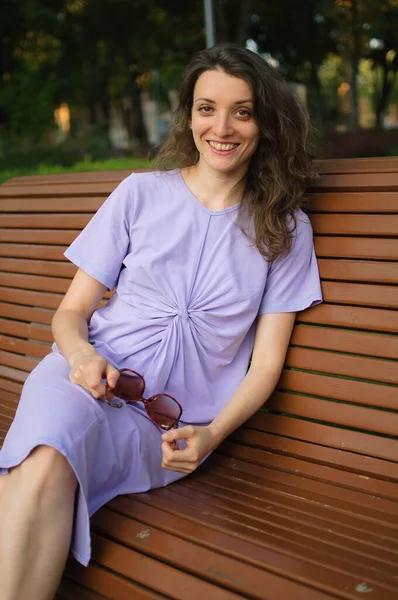 Chica joven en vestido violeta claro está teniendo gran tiempo durante las vacaciones en el verano sentado en el banco, concepto de viaje — Foto de Stock