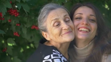 Gözlüklü mutlu kıdemli anne yetişkin kızına sarılıyor, kadınlar birlikte eğleniyor, farklı nesillerden gelen samimi aile dışarıda eğleniyor.