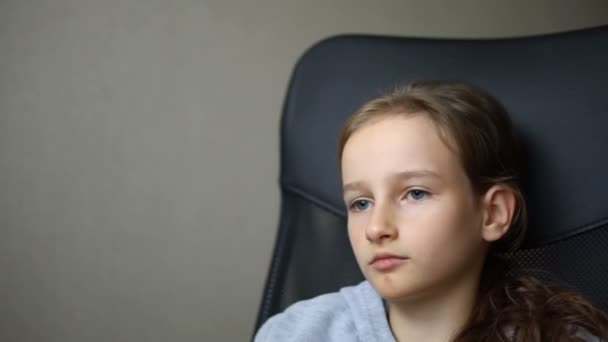 Маленька сумна дівчинка сидить на чорному офісному стільці, покарання, серйозне обличчя — стокове відео
