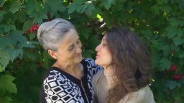 Gözlüklü mutlu kıdemli anne yetişkin kızına sarılıyor, kadınlar birlikte eğleniyor, farklı nesillerden gelen samimi aile dışarıda eğleniyor.