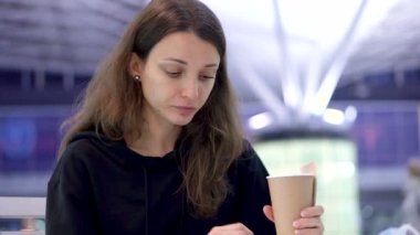 Elinde bir fincan kahve tutan bir kız. Genç kız taze kruvasan yiyor ve kafedeki, havaalanındaki ya da tren istasyonundaki kağıt bardaktan içecek içiyor.