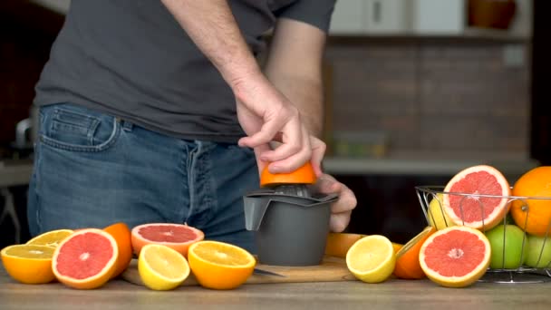 Um homem espreme sumo de laranja com sumo cítrico. Close-up de mãos, laranjas, juicer, estilo de vida saudável — Vídeo de Stock