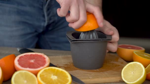 Muž vymačká pomerančový džus z citrusového džusu. Detailní záběr na ruce, pomeranče, odšťavňovač, zdravý životní styl — Stock video