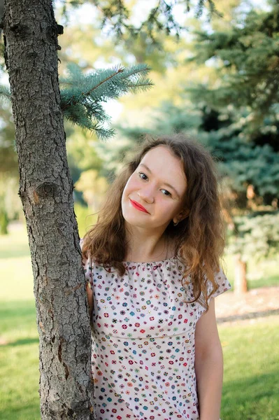 Jong brunette meisje in jurk is poseren op boom achtergrond in de zomer in park — Stockfoto