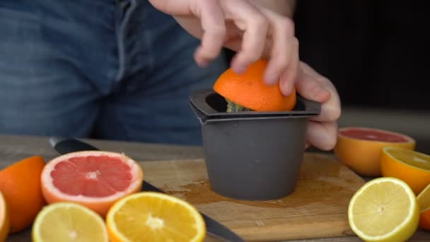 Een man perst sinaasappelsap met citrussap. Close-up van handen, sinaasappels, sapcentrifuge, gezonde levensstijl — Stockvideo