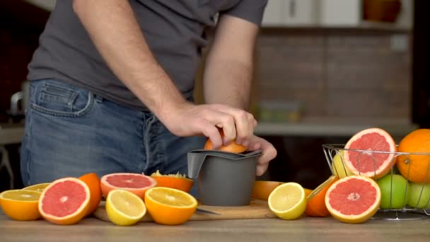 男は柑橘系のジューサーでオレンジジュースを絞る。手、オレンジ、ジューサー、健康的なライフスタイルのクローズアップ — ストック動画