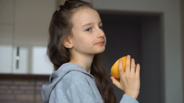 Niña con el pelo largo está lamiendo la mitad de la naranja. Feliz infancia, alimentación saludable — Vídeos de Stock