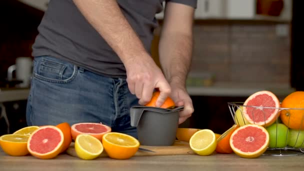 Egy férfi narancslevet présel citrusfacsaróval. Kéz, narancs, gyümölcsfacsaró, egészséges életmód — Stock videók