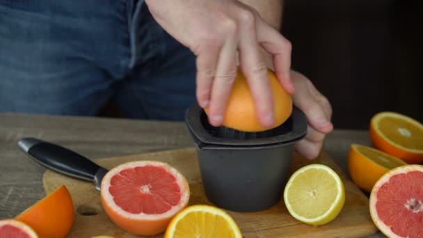 Ένας άντρας συμπιέζει χυμό πορτοκαλιού με χυμό εσπεριδοειδών. Κοντινό πλάνο των χεριών, πορτοκάλια, αποχυμωτής, υγιεινό τρόπο ζωής — Αρχείο Βίντεο