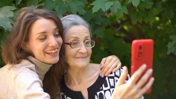 Filha adulta e mãe sênior estão tirando foto de auto-retrato, selfie no smartphone vermelho juntos, aposentadoria feliz, conceitos do dia das mães. — Vídeo de Stock