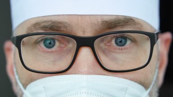 Müde ernstzunehmende männliche Berufsarzt in Maske, Brille und Schutzanzug nach der Einnahme einer großen Anzahl von Patienten aufgrund der Coronavirus-Epidemie. — Stockvideo