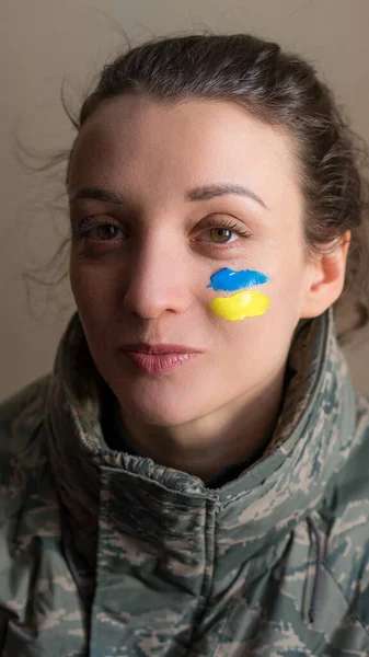 Крытый портрет молодой девушки с сине-желтым украинским флагом на щеке в военной форме, обязательная воинская повинность в Украине, концепции равенства — стоковое фото