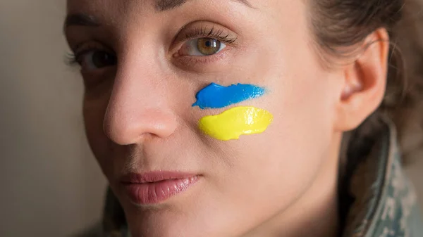Inomhus porträtt av ung flicka med blå och gul ukrainska flagga på kinden bär militär uniform, obligatorisk värnplikt i Ukraina, jämställdhet begrepp Royaltyfria Stockbilder
