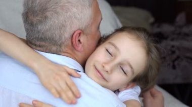 Yetişkin baba ve küçük sarışın kızın aile portresi. Babalar gününü kutlarken evde sarılıyorlar.