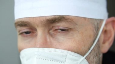 Koronavirüs salgını nedeniyle çok sayıda hasta aldıktan sonra maskeli, gözlüklü ve koruyucu süitli ciddi bir yetişkin erkek doktor yorgun düştü..