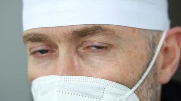 Trött allvarlig mogen manlig professionell läkare i mask, glasögon och skyddande svit efter att ha tagit ett stort antal patienter på grund av epidemin av coronavirus. — Stockvideo