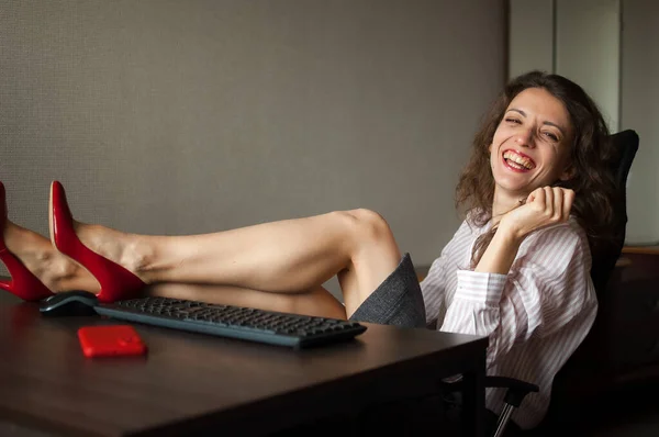 Ofis masasında dizüstü bilgisayarlı esmer Portriat, yüksek topuklu kırmızı ayakkabılı seksi kadın masada oturuyor. Baştan çıkarıcı sekreter kavramı, kadın modası, işte rahatla. — Stok fotoğraf