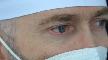 Koronavirüs salgını nedeniyle çok sayıda hasta aldıktan sonra maskeli, gözlüklü ve koruyucu süitli ciddi bir yetişkin erkek doktor yorgun düştü..