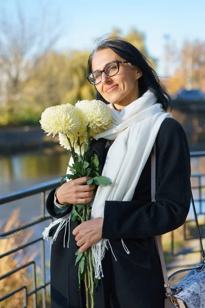 Uma bela mulher de meia-idade ficando grisalho em um casaco escuro em uma cidade de primavera com um buquê de flores. — Fotografia de Stock