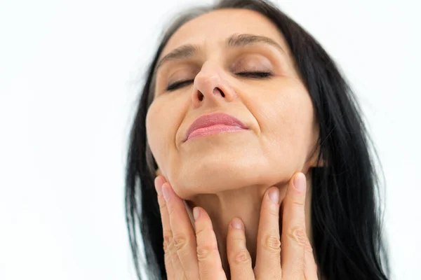 Retrato de cerca de una mujer de mediana edad que comienza a ponerse canoso sobre un fondo blanco, belleza del cuidado de la piel de la cara, cosméticos para el cuidado de la piel de mediana edad, concepto de cosmetología. Fotos de stock libres de derechos