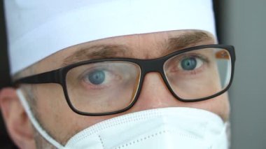 Koronavirüs salgını nedeniyle çok sayıda hasta aldıktan sonra maskeli, gözlüklü ve koruyucu süitli ciddi bir yetişkin erkek doktor yorgun düştü..
