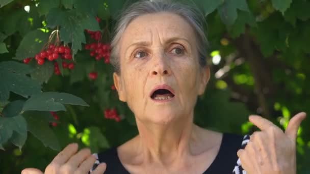 Втомлена старша сіра волохата жінка почувається погано через менопаузу, концепцію менопаузи, що стоїть біля зеленого дерева — стокове відео