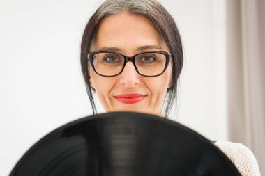 Stüdyo fotoğrafında orta yaşlı bir kadın gri saçlı, siyah beyaz giysili, plastikten plaklı beyaz elbiseli orta yaşlı, seksi bir kadın, mutlu bir hayat konsepti var.