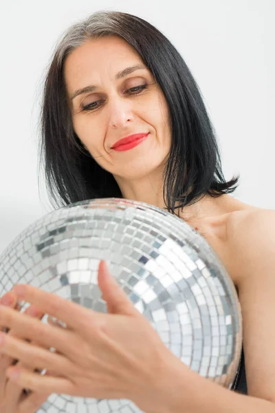Stüdyo fotoğrafında orta yaşlı bir kadın gri saçlı, gümüş renkli disko topuyla beyaz arka planda, orta yaşlı seksi bir kadın, mutlu bir hayat konsepti. — Stok fotoğraf