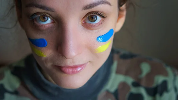 Indoor portrait of young girl with blue and yellow ukrainian flag on her cheek wearing military uniform, mandatory conscription in Ukraine, equality concepts Stock Image
