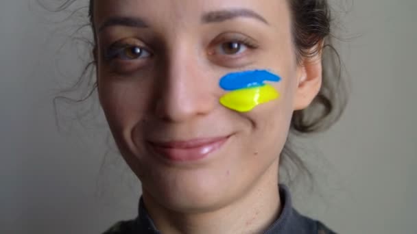 Retrato interior de niña con bandera ucraniana azul y amarilla en la mejilla con uniforme militar, reclutamiento obligatorio en Ucrania, conceptos de igualdad — Vídeos de Stock