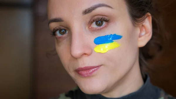 Inomhus porträtt av ung flicka med blå och gul ukrainska flagga på kinden bär militär uniform, obligatorisk värnplikt i Ukraina, jämställdhet begrepp Royaltyfria Stockfoton