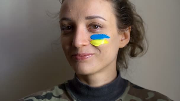 Beltéri portré fiatal lány kék és sárga ukrán zászló az arcán visel katonai egyenruha, kötelező besorozás Ukrajnában, egyenlőség fogalmak — Stock videók