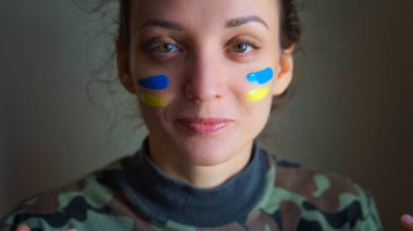 Yanağında mavi ve sarı Ukrayna bayrağı, askeri üniforma, Ukrayna 'da zorunlu askere alınma, eşitlik kavramları olan genç bir kızın kapalı bir portresi.