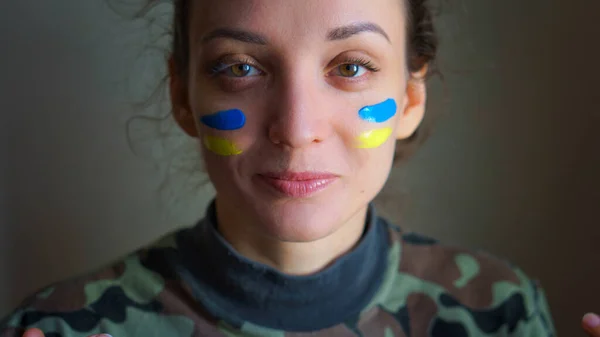 Retrato interior de niña con bandera ucraniana azul y amarilla en la mejilla con uniforme militar, reclutamiento obligatorio en Ucrania, conceptos de igualdad Imágenes de stock libres de derechos