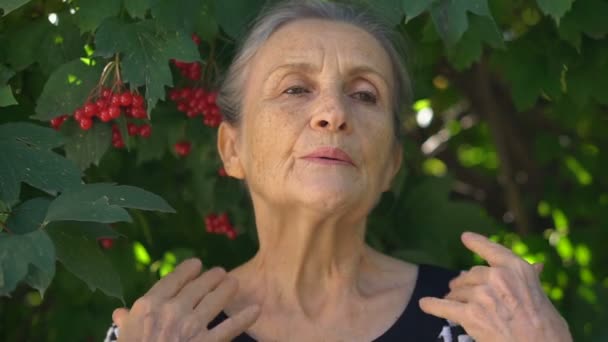 Yaşlı, yaşlı, gri saçlı kadın menopoz ve yeşil ağacın yanında duran menopoz rahatlama konsepti yüzünden kendini kötü hissediyor. — Stok video