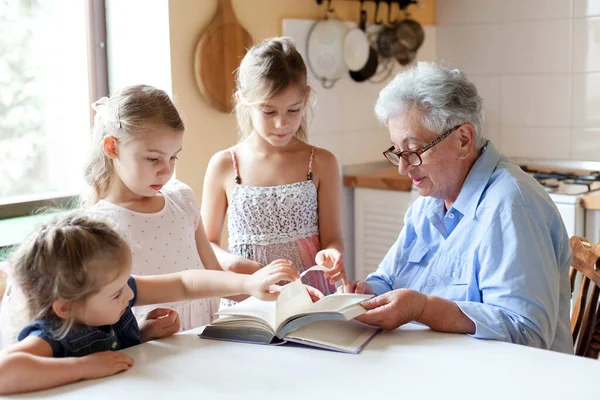 Kids and grandmother read book aloud at home kitchen. Happy family have fun.