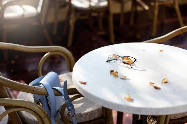 Autumn cafe outdoors. Eyeglasses and fallen leaves on table in cozy street restaurant. Still life with relaxing mood. Lifestyle moments, slow life.