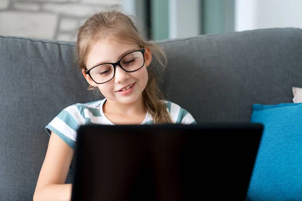 Child in glasses using laptop at home. Happy school girl in video call at lesson. Distance learning, online education in virtual class. Homeschooling, communication, connection in covid quarantine.