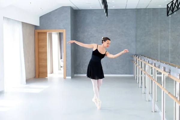 Ballerina dancing in ballet studio on pointe shoes. Workout in ballet class room in classical school. Professional dancer doing exercises near barre, mirror. Graceful woman has modern dance practice.