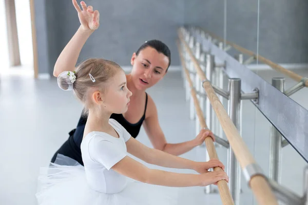 Ballet teacher and little ballerina in classical dance school. Barre workout. Female trainer teaching kid. Child girl studying in choreographic studio. Support in practicing for children.