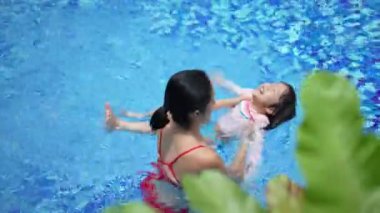 Asyalı kadın anne ve çocuk yüzme havuzunda yüzmeyi öğreniyorlar.