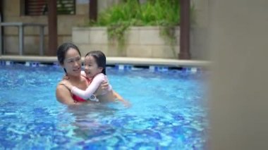 Asyalı kadın anne ve çocuk yüzme havuzunda yüzmeyi öğreniyorlar.