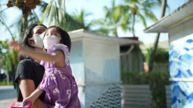 Asian Asia mother carrying daughter walking at sentosa, Singapore with mask on