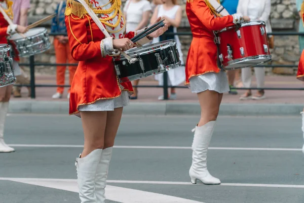 Street performance of festive march of drummers girls in red costumes on city street. Young girls drummer in red vintage uniform at the parade