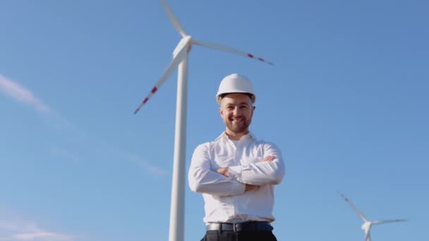 Lufttechnik-Ingenieur steht in Business-Kleidung und weißem Helm vor Windmühlenhintergrund — Stockvideo