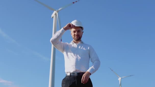 Ingénieur de puissance aérienne se tient dans des vêtements de style d'affaires et casque blanc sur un fond de moulin à vent — Video