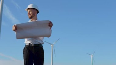 Beyaz kasklı ve klasik gömlekli bir erkek mühendis elektrik santrallerinin kapasitesini inceler ve büyük bir sayfa kağıt üzerinde proje çizimlerini okur.