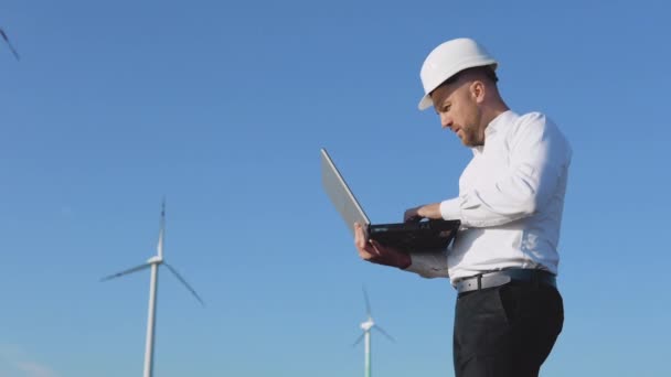 Инженер-мужчина в белом шлеме и в классической рубашке проверяет мощность электростанций и делает заметки в ноутбуке — стоковое видео